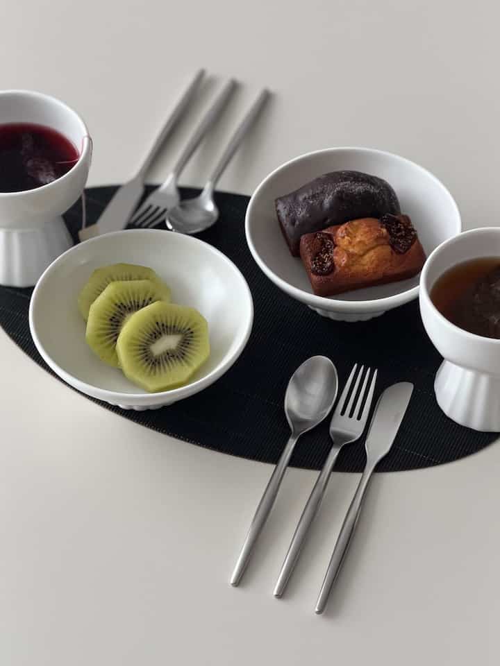 シンプルで清潔感のあるホワイトトーンのテーブルに食器と果物、お茶が配置されたミニマルな印象のホームカフェ空間