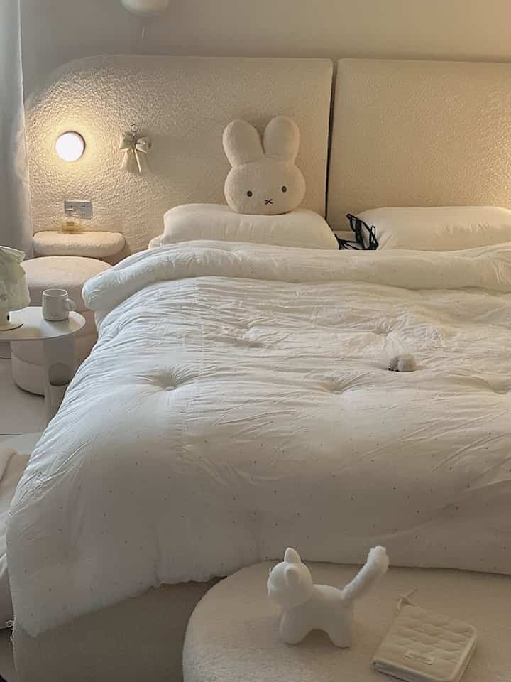 ナチュラルカラートーンとホワイトの寝室、ふわふわのベッドとぬいぐるみが配置された雰囲気のあるインテリア