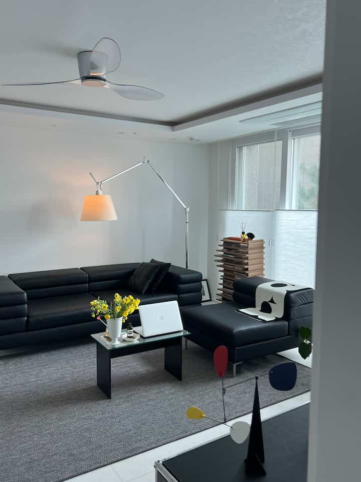 白い壁と黒のコーナーソファが配置されたモダンな二人暮らしのリビング、抜け感のあるレイアウトとフロアランプが特徴的な空間