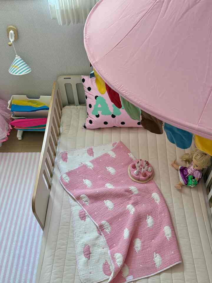 ピンクトーンの子供部屋、子供用ベッドにドット柄のピンク枕、ピンクのキャノピーとブランケットがかわいらしく配置されたインテリア