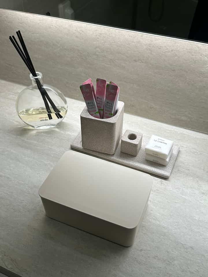 ベージュとアイボリーの色調のバスルーム、柔らかな照明の下で整然と配置された小物とディフューザーがある印象的な空間