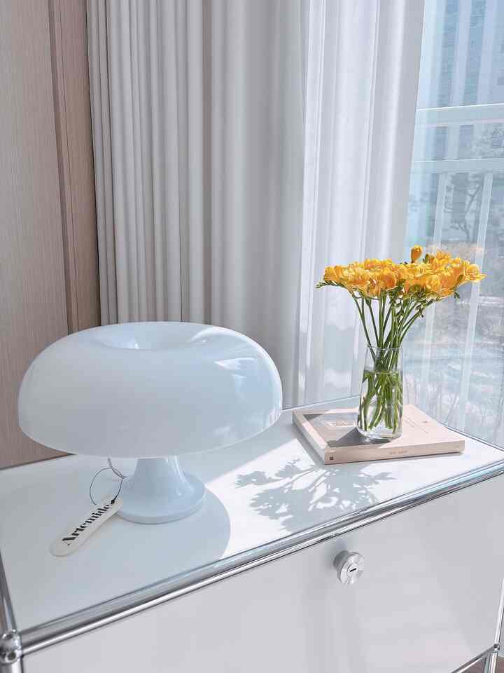 明るい白を基調としたモジュール型キャビネットの上にアルテミデのテーブルランプと黄色いフリージアの花瓶が置かれた清潔感のあるインテリア