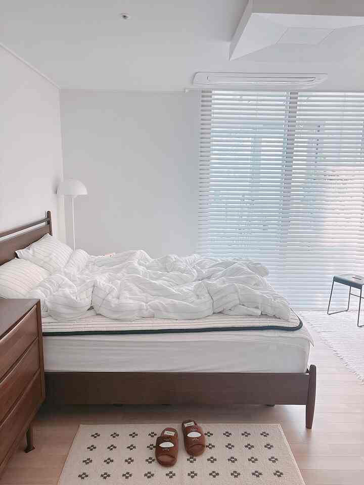 ホワイトとブラウンのトーンの寝室、木製ベッドとスツール、ブラインドが配置されたモダンで清潔感のある空間