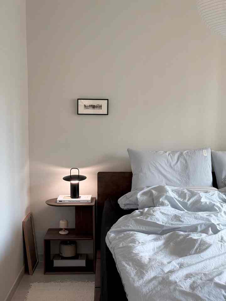 White and brown toned bedroom featuring a nightstand and lamp with a simple, natural atmosphere