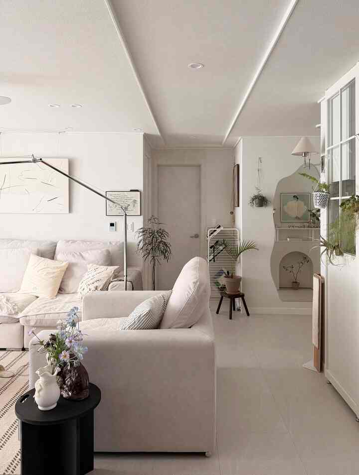 ベージュとホワイトの色調のリビング、ファブリック製の大きなソファと額縁、ハンギングプラントが配置された自然で清潔感のあるインテリア