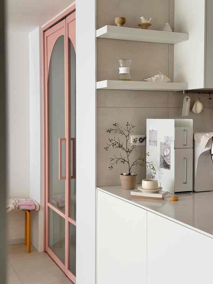 ベージュとホワイトの色調のキッチン、シンプルな棚とカップ、植物の小物が配置された落ち着きのあるインテリア