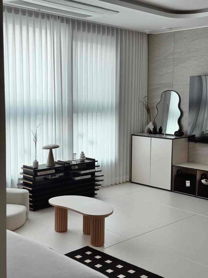 White-toned living room featuring a kidney-shaped coffee table and elegant wavy mirror, presenting a modern and minimal atmosphere