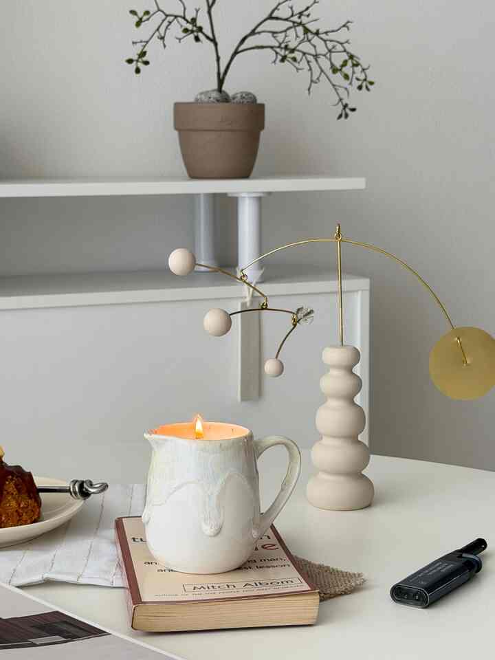 白とベージュのトーンの狭いダイニングスペース、灯されたキャンドル入りカップと自然素材のオブジェが調和した雰囲気のあるインテリア