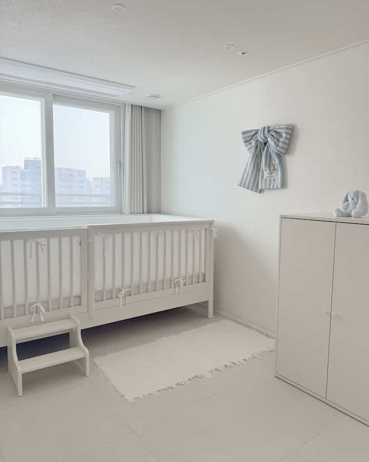 明るいホワイトトーンの子供部屋、白いベビーベッドとシンプルなインテリアが配置された清潔感のある空間