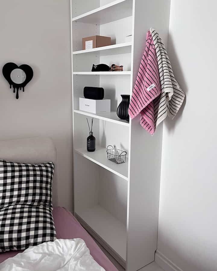 ホワイトとピンクのトーンのシンプルな寝室、壁に並ぶ白い本棚が配置された雰囲気のある空間