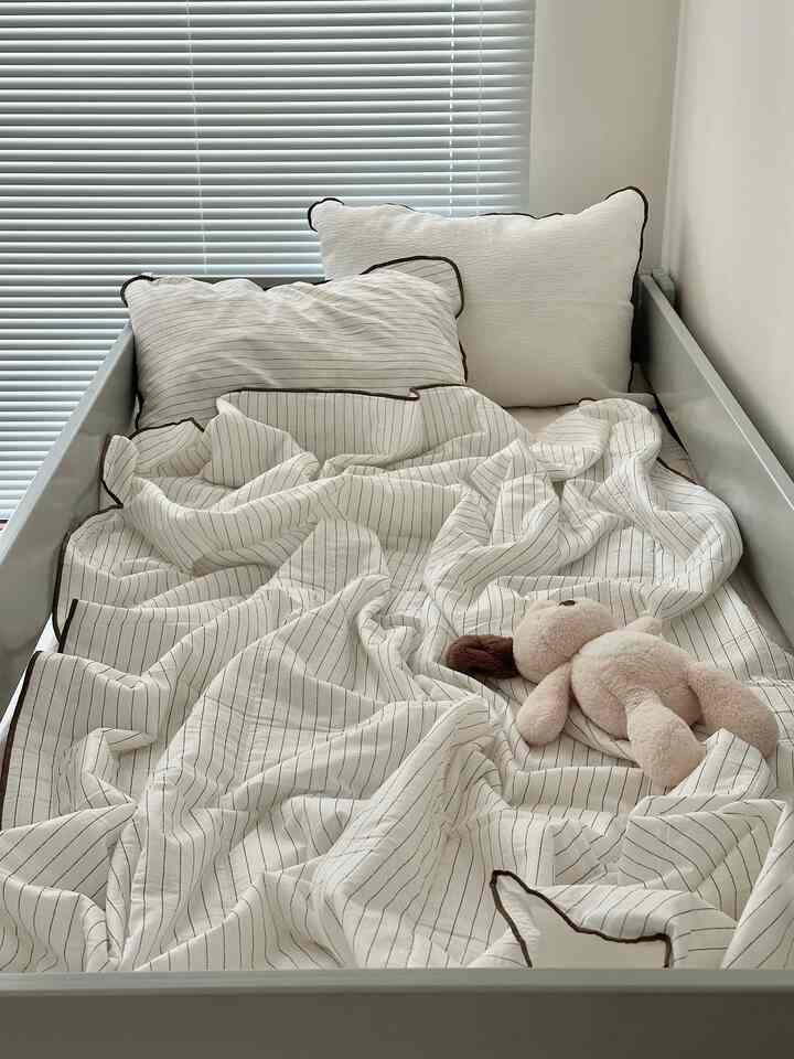 ナチュラルカラーの子供部屋風寝室、白と茶色のストライプ柄の寝具と枕が配置された整ったベッド空間