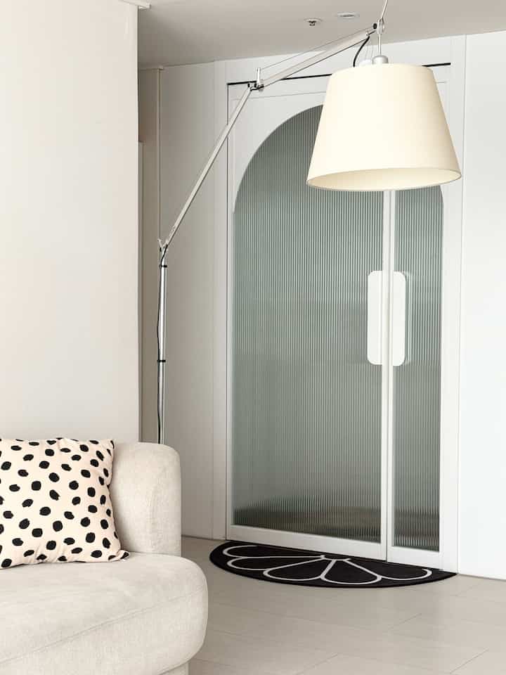 白と黒の調和が取れたモダンな玄関、ベージュのソファとフロアランプが配置されたすっきりとしたインテリア