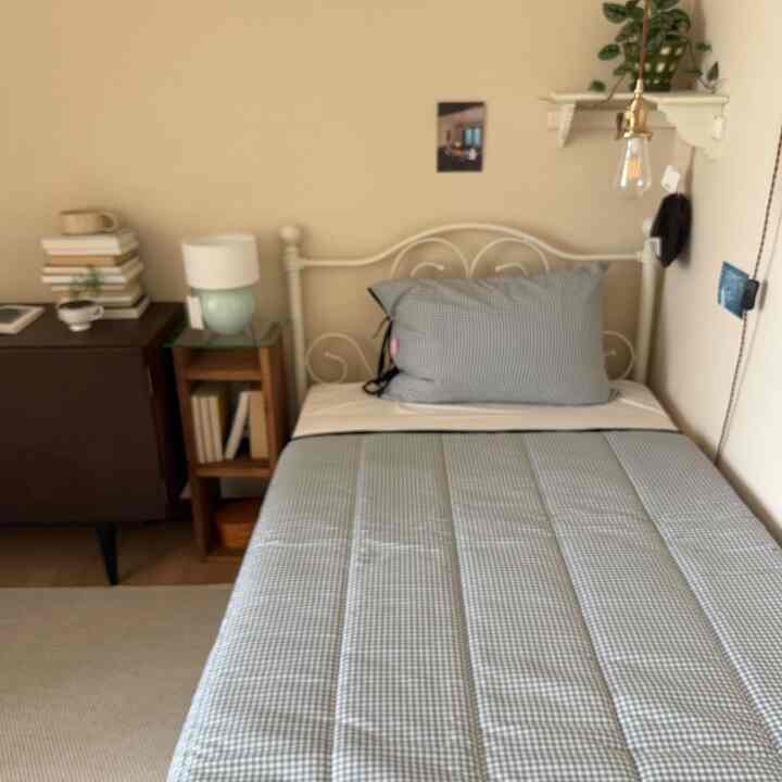 ベージュの壁とナチュラルトーンの6畳寝室、中央にメタルフレームのシングルベッドとパステルブルーのチェック柄寝具が配置されたシンプルなインテリア