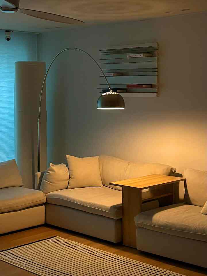 暖かいベージュトーンのリビング、ナチュラルモダンスタイルのベージュソファと木製サイドテーブル、フロアランプとストライプのラグが置かれた印象的な空間