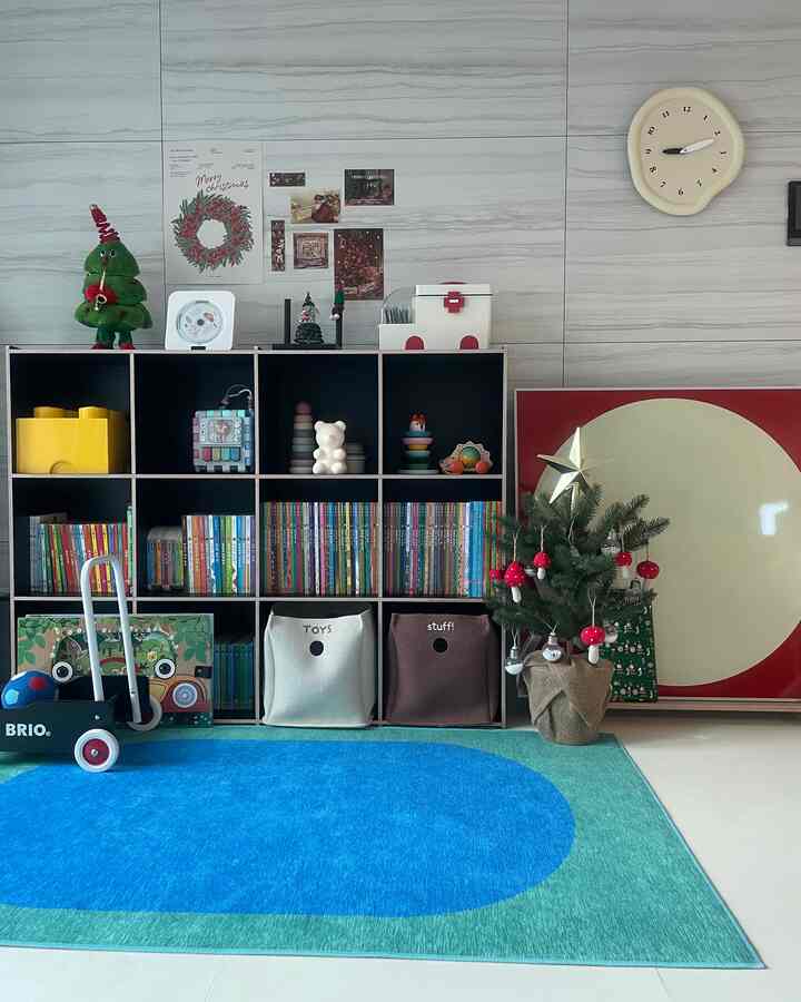 明るいグレーの壁と黒い本棚に子供のおもちゃや本が整頓された子供部屋、青と緑のラグが敷かれた暖かみのある空間
