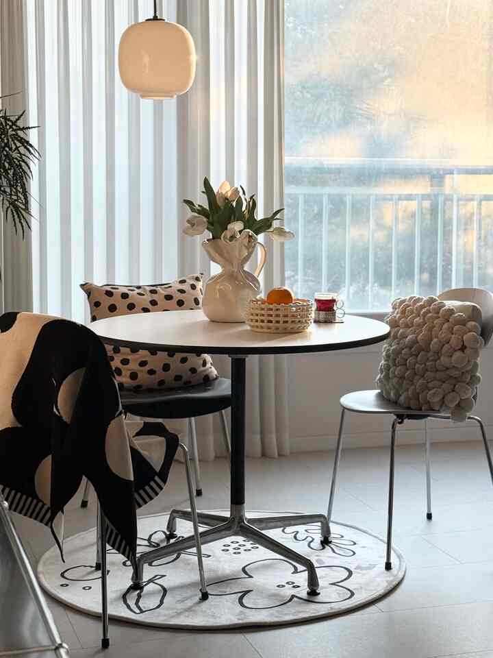 白と黒のトーンが調和したダイニングルーム、丸テーブルと個性的なクッションが配置されたモダンな空間