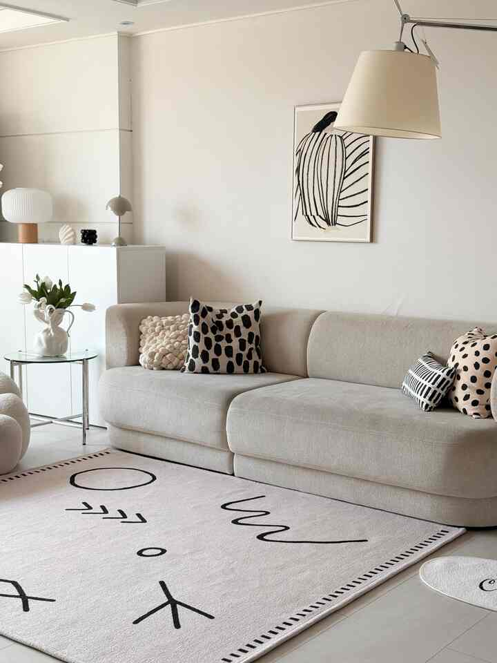 白とベージュの色調のリビング、ベージュのソファにパターンのクッションと抽象的なウォールアートが配置されたシンプルなインテリア