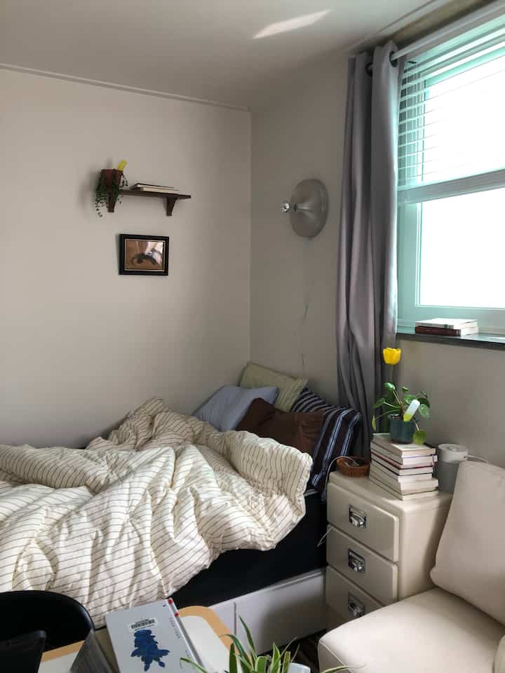 Natural-toned bedroom featuring bed with pillows, nightstand, and wall shelf creating a cozy atmosphere