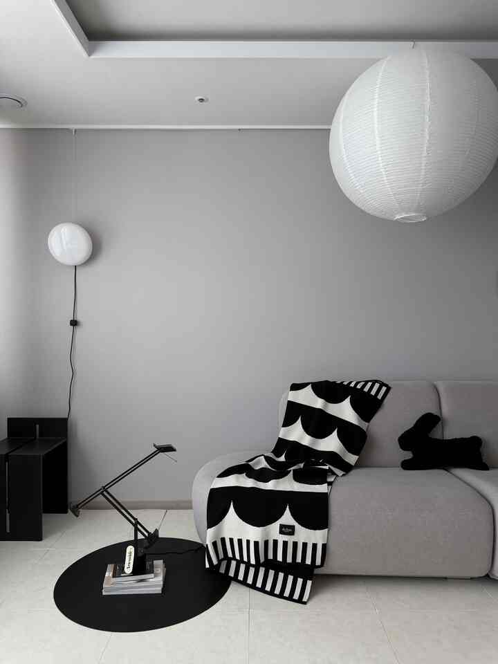モノトーンの黒と白が対比するモダンなリビング、シンプルなソファとパターンのスロー、テーブルランプが配置された印象的な空間