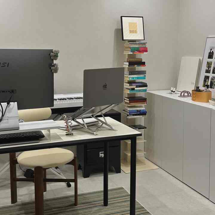 A white and wood-tone study space featuring desk, monitor stand, and a unique floating bookshelf providing clean home office setup