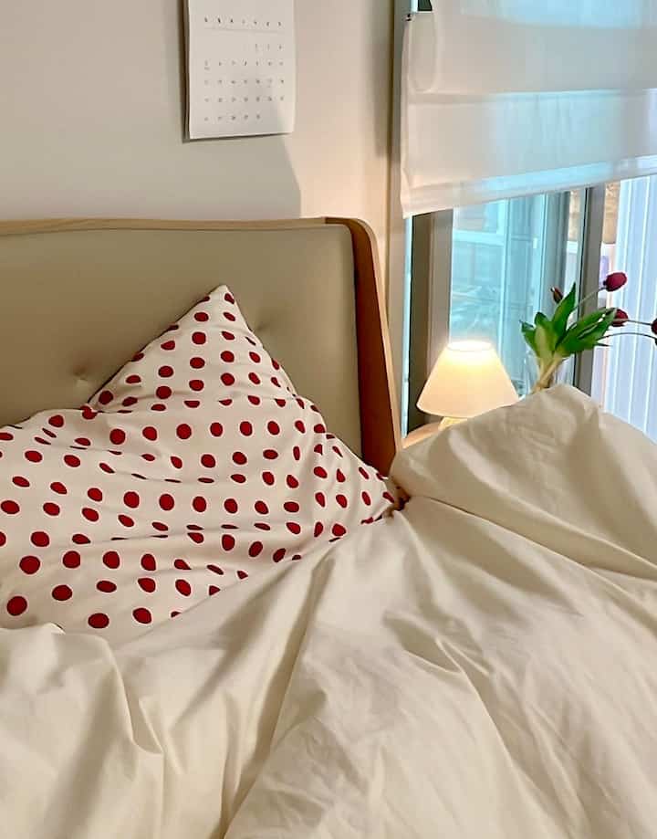 ベージュ色の寝室、赤い水玉模様の枕と白い掛け布団カバーが配置されたシンプルモダンなインテリア