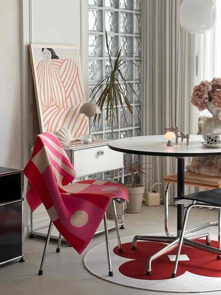 明るい白色が基調のリビングに、赤い模様のブランケットが掛けられた椅子と丸テーブル、ラグが配置されたカフェ風のインテリア