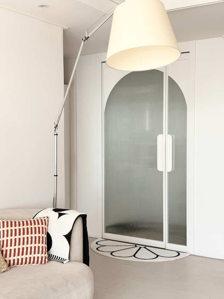 白とベージュの色調の玄関空間、シンプルなソファとフロアランプ、半円形のラグが配置されたナチュラルな雰囲気のインテリア