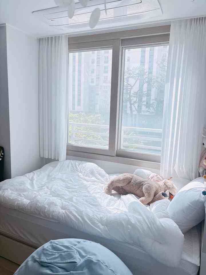 ホワイトとパステル調の子供部屋、大きな窓と白いカーテン、ベッドの上に犬のぬいぐるみとビーズクッションが置かれた温かみのある空間