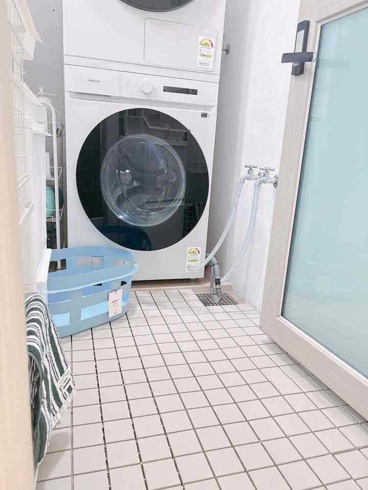 白を基調としたタイル床のランドリールーム、洗濯機と青いランドリーバスケットが配置された清潔感のある空間