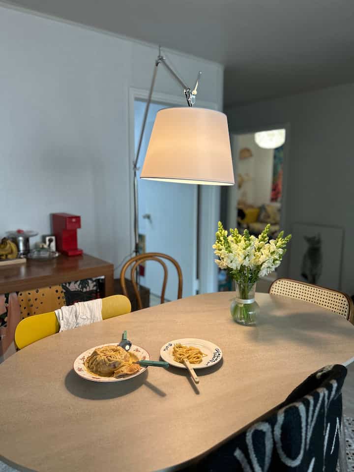 White-walled dining room with wood-tone furniture, featuring a vase with flowers and warm lighting over the dining table