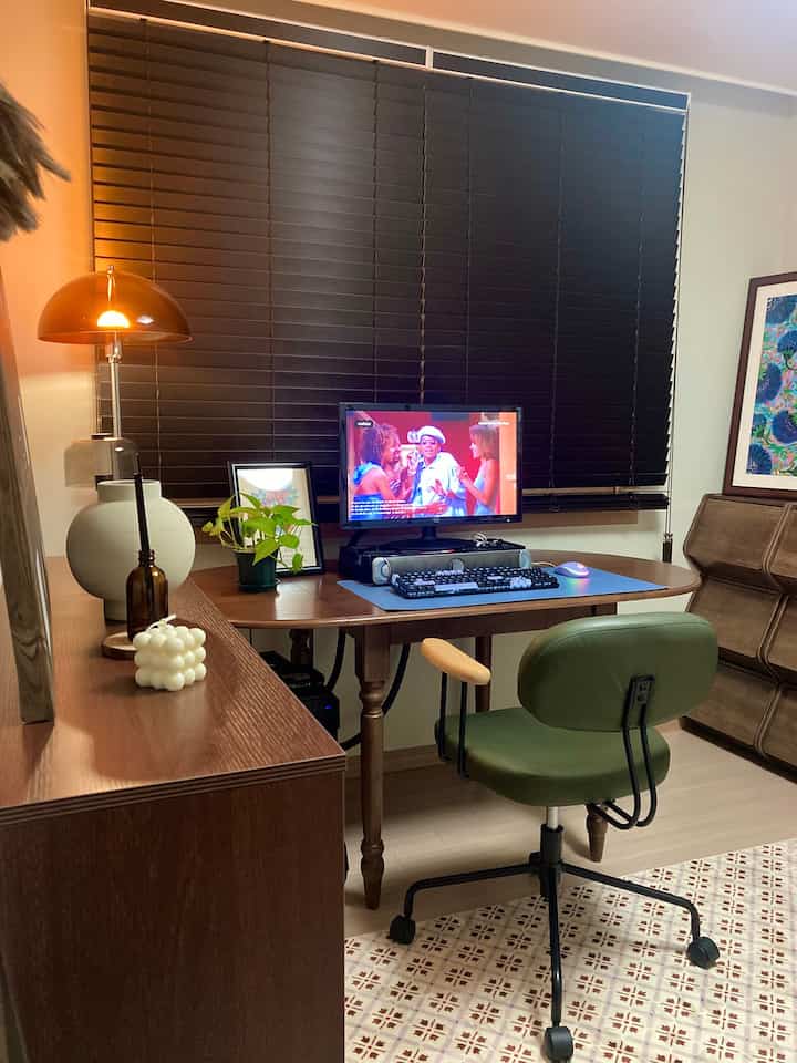 濃い木目調の書斎、グリーンレザーのオフィスチェアと木製デスクに照明とモニターが配された雰囲気のあるインテリア