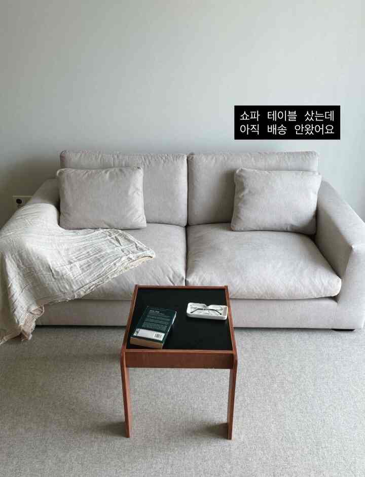 ライトグレーのリビング、中央に3人掛けソファと前に小さな木製サイドテーブルが配置されたミニマルなインテリア空間