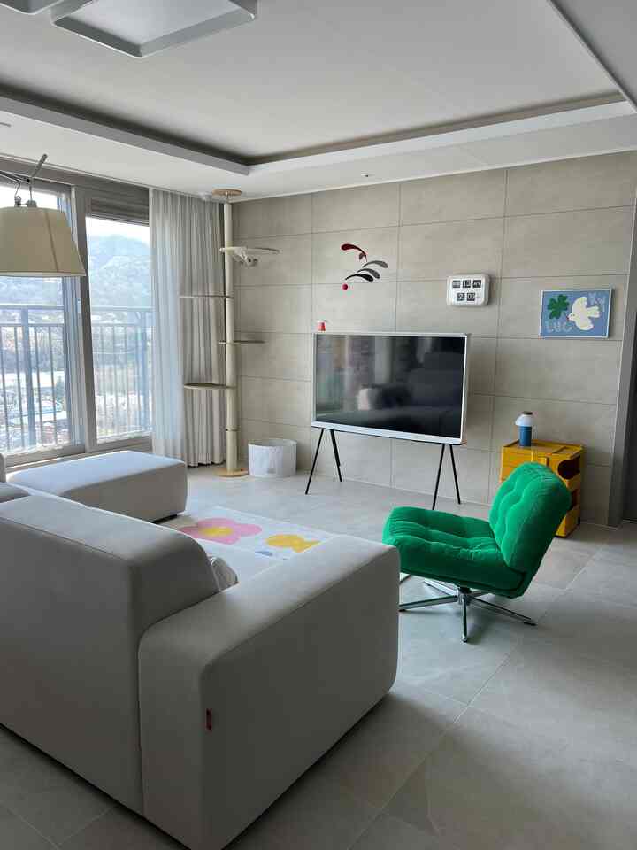 白とナチュラルトーンのリビング、ソファとキャットタワー、テレビ台が配置された落ち着いたモダンな空間