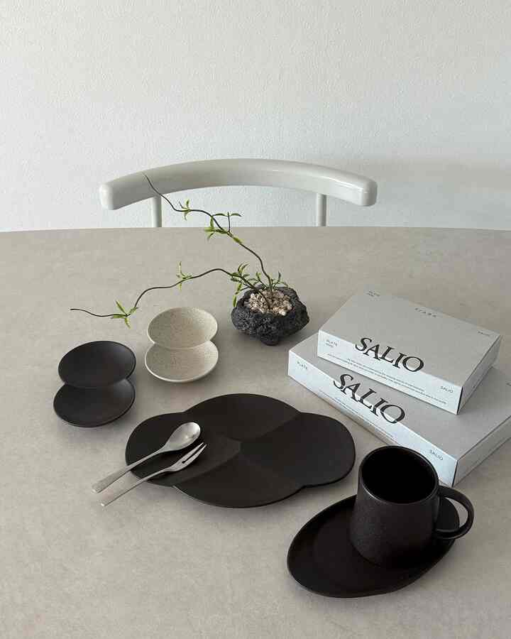 白い壁とダイニングチェアのあるキッチン空間、ブラックとベージュの食器とマグカップがテーブルに整然と並ぶ落ち着いたおうちカフェの雰囲気のインテリア