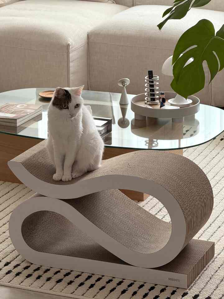 ナチュラルなベージュ色調のリビング、爪とぎチェアに座る猫が配置された落ち着いた雰囲気のインテリア