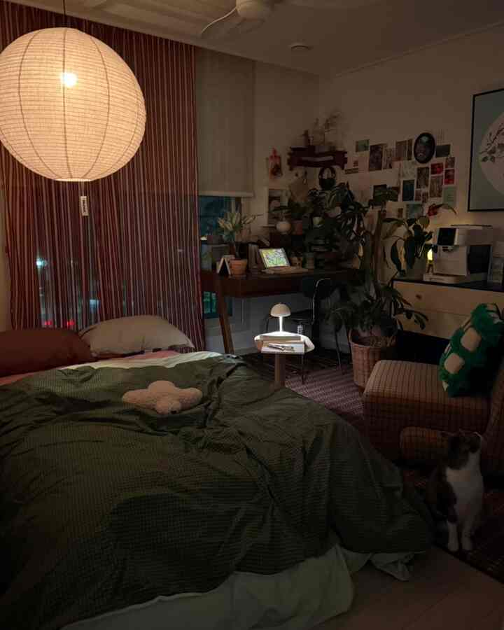 暖かな照明が灯る寝室、緑の寝具とミニテーブル、ペットの猫がいる居心地の良い空間