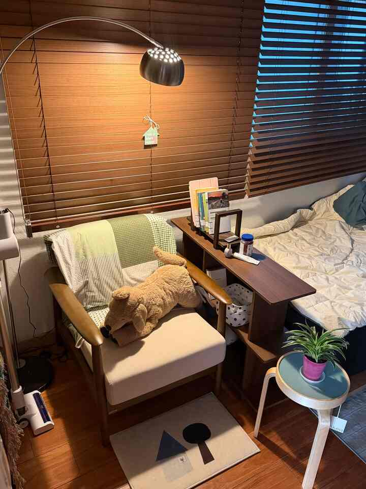 木目調のブラインドとナチュラル素材の家具が配置された落ち着いた一人暮らしの寝室。