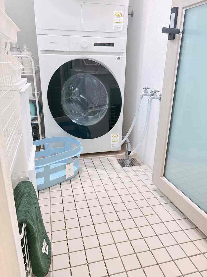 白と青の色調の洗濯室、中央にサムスンの洗濯機が配置され、青いバスケットと緑のタオルが整然と置かれた雰囲気のあるインテリア