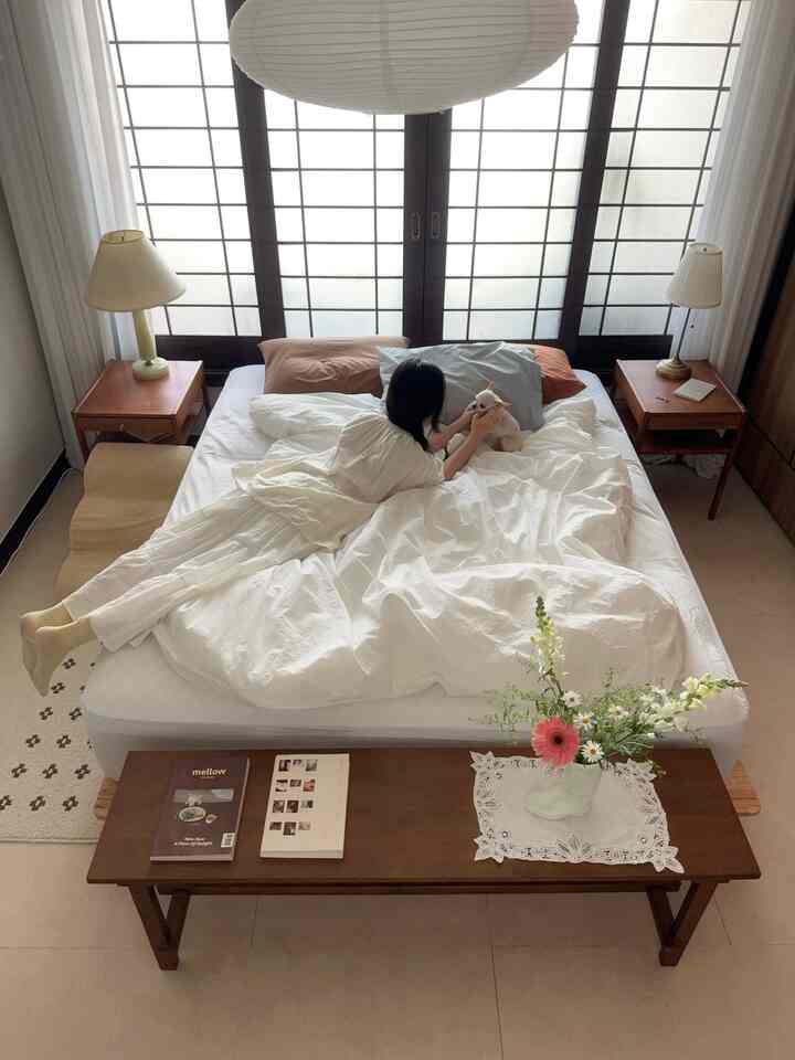 明るくナチュラルな白と木目調が調和した寝室、ベッドの上で犬と一緒に横たわる人がいる雰囲気のある空間