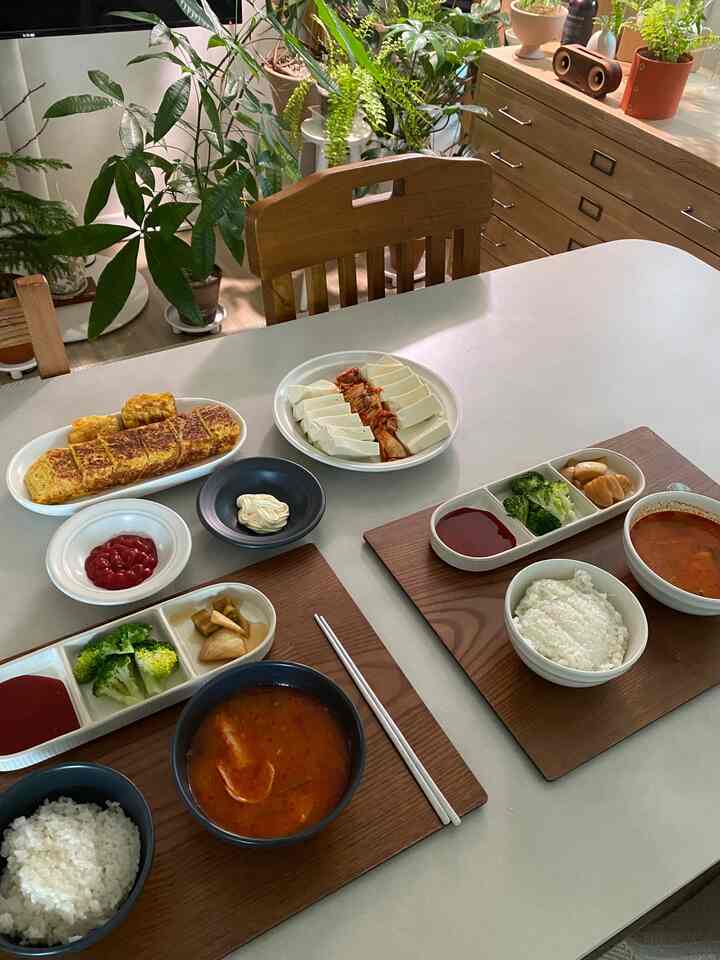 ナチュラルな木目調と植物が配置されたダイニングスペース、食卓にはシンプルな韓国料理が並ぶ雰囲気のあるインテリア