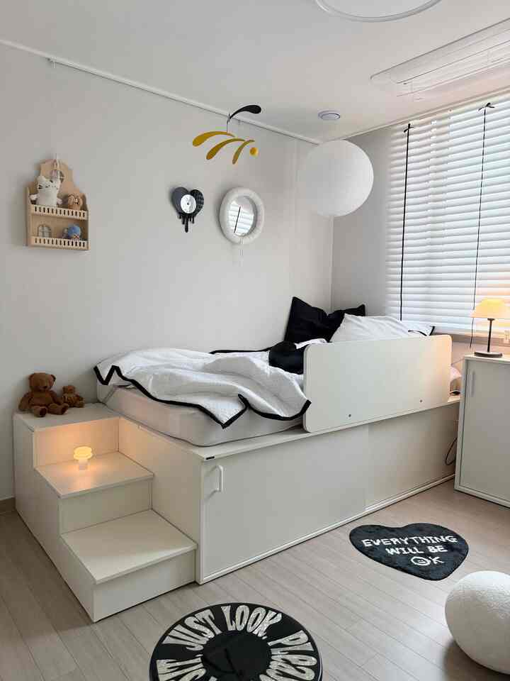 ホワイトトーンの子供部屋、収納ベッド、モダンな照明、壁掛け時計と鏡が配置されたすっきりとした空間