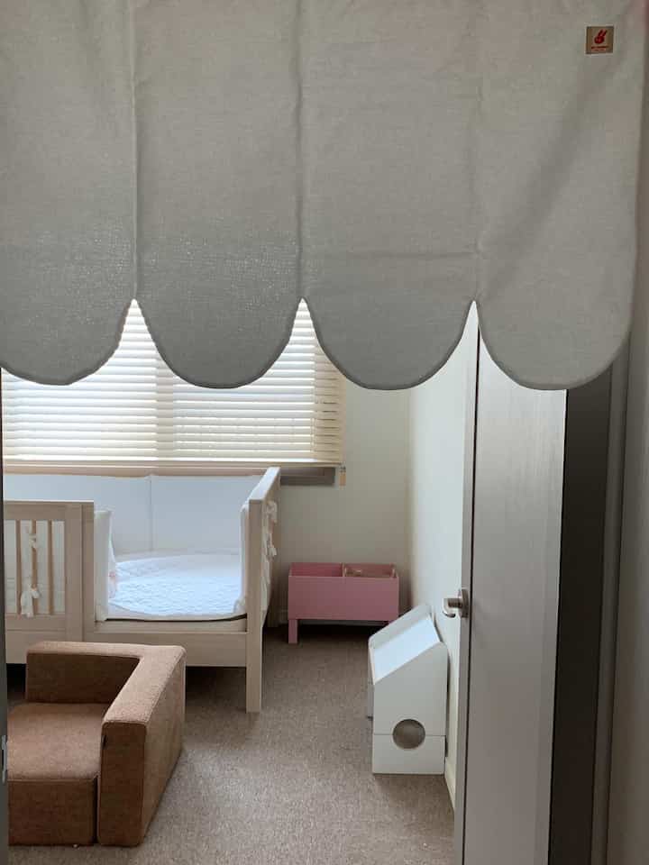 白と茶色のトーンの子供部屋、子供用ベッドやソファ、ブラインドとカーテンが配置された雰囲気のあるインテリア
