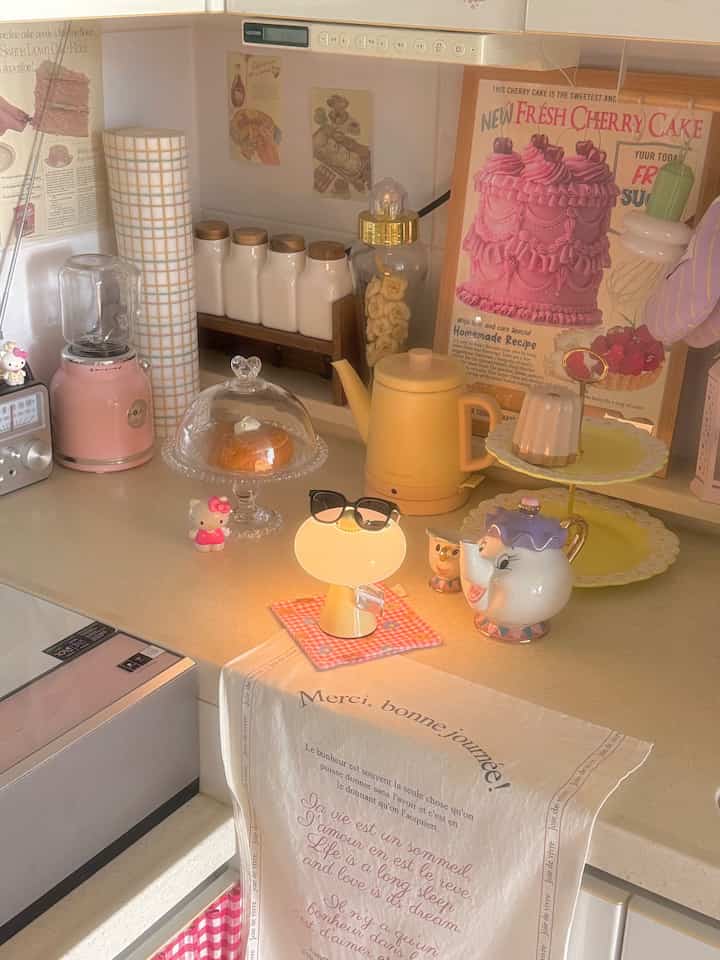 ピンクとイエローの調和がある居心地の良いキッチン、ビンテージポスターと多彩なホームカフェアイテムが配置された温かみのあるインテリア