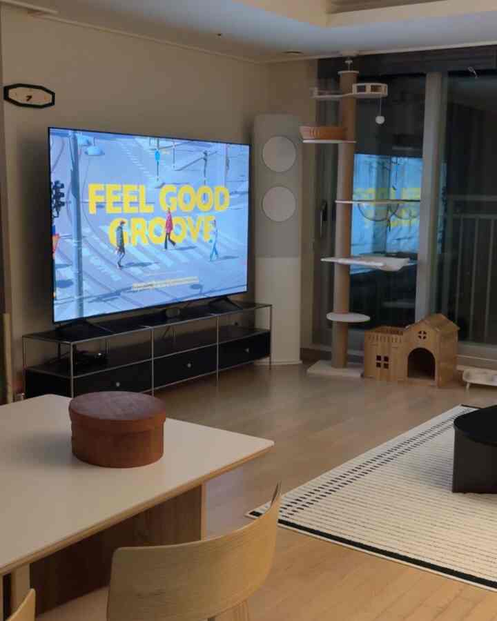 白と木目調が調和したリビング、ミッドセンチュリーモダンのインテリアに大きなキャットタワーとテレビ台が配置された空間