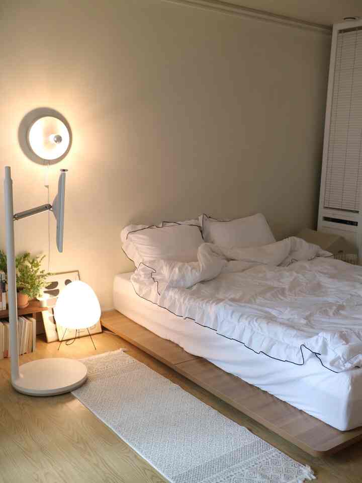 白と木目調の寝室、低床ベッドと寝具、柔らかな照明が配置された落ち着いた雰囲気のインテリア