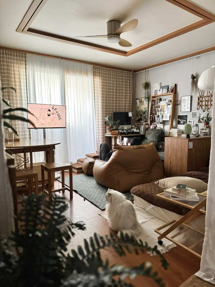 木目調とブラウンが調和したリビングルーム、チェック柄のカーテンとビーンバッグソファ、そして猫が二匹いる暖かい雰囲気のインテリア