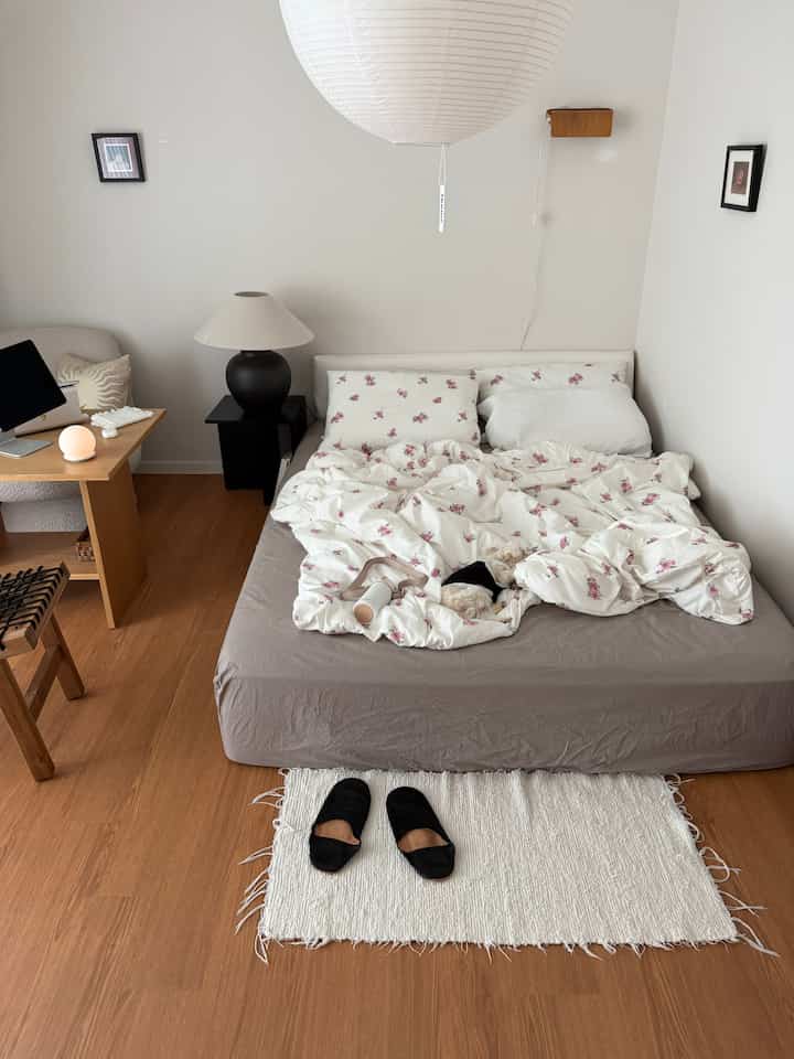 White-walled bedroom with brown flooring featuring floral bedding and a small dog resting, creating a cozy atmosphere
