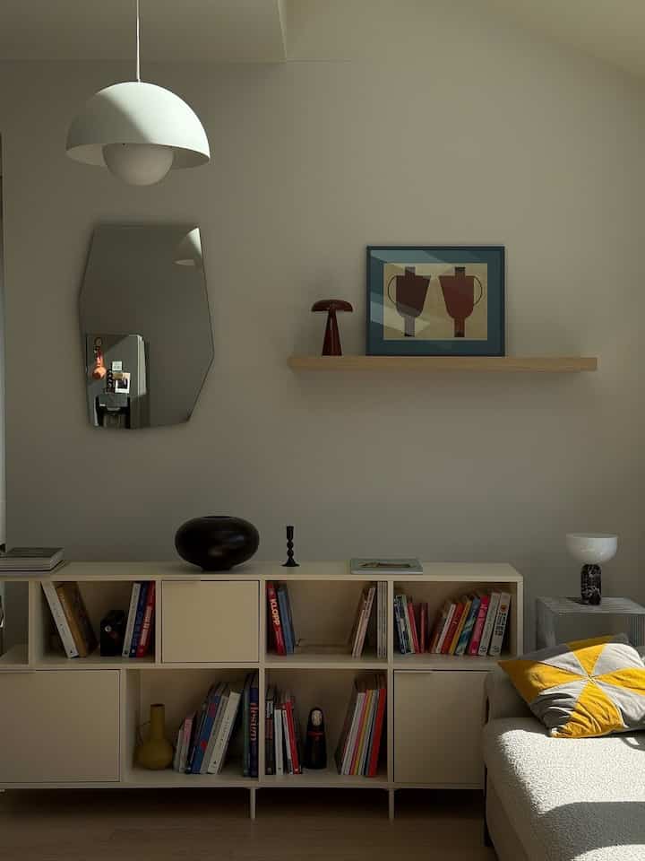 A quiet living room with just the right amount of personality. Warm neutral walls, sculptural lighting, and a well-loved bookshelf create an easy, lived-in feel, while the graphic artwork and mustard pillow bring in subtle color and contrast. Thoughtful styling keeps the room calm without making it feel too polished.

Credit: @joyceemli

#LivingRoom #InteriorInspiration #WarmMinimalism #ModernInterior #CozyLiving #HomeStyling #DesignDetails #BookshelfStyling #SculpturalLighting #NeutralHome #CuratedHome #EverydayInteriors #ModernHome #ArtworkAtHome #ApartmentDecor