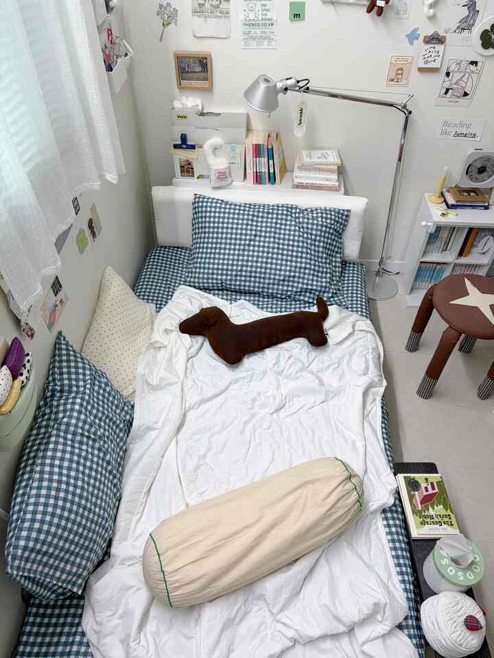 ホワイトとブルーのトーンの狭い寝室、ギンガムチェックの枕と白い寝具が配置された落ち着いた空間