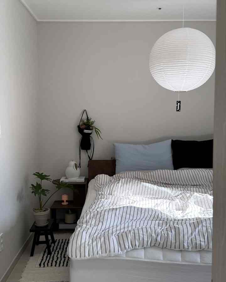 Bright gray-walled bedroom with white bedspread, accented by black cushions and furniture creating a clean atmosphere